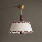 Unlit Clérachic pleated ceiling light with a tapered white shade, wavy brown trim and a wood bead, against a taupe wall.