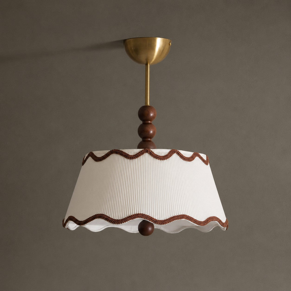Unlit Clérachic pleated ceiling light with a tapered white shade, wavy brown trim and a wood bead, against a taupe wall.