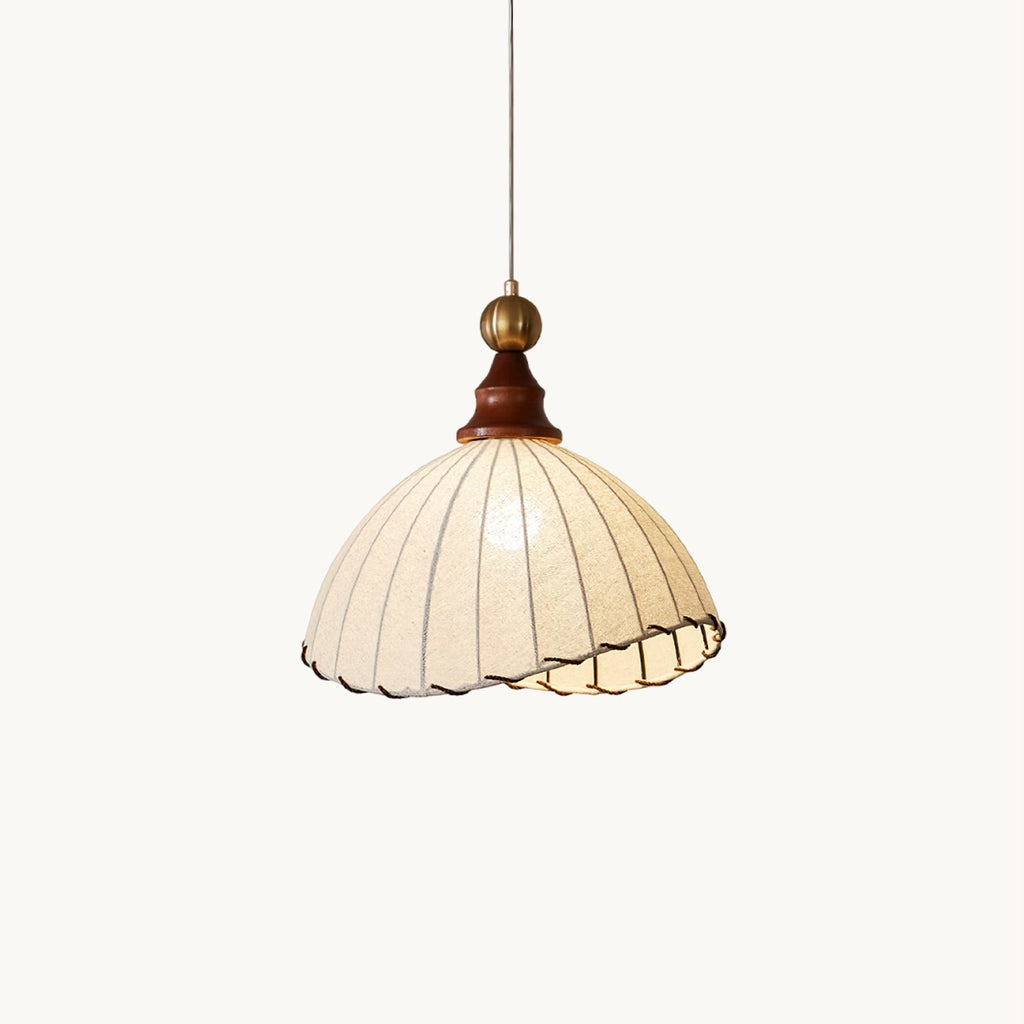 A beige pleated fabric Clérachic pendant light with a walnut cap and brass ball, hanging on a plain white backdrop.