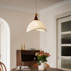This Clérachic pendant light hangs in a dining room with an arched doorway, above a walnut cabinet and a vase of orange roses.
