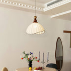 A Clérachic pendant light with a scalloped beige shade, hanging below a ceiling cornice beside an oval mirror and candlesticks.