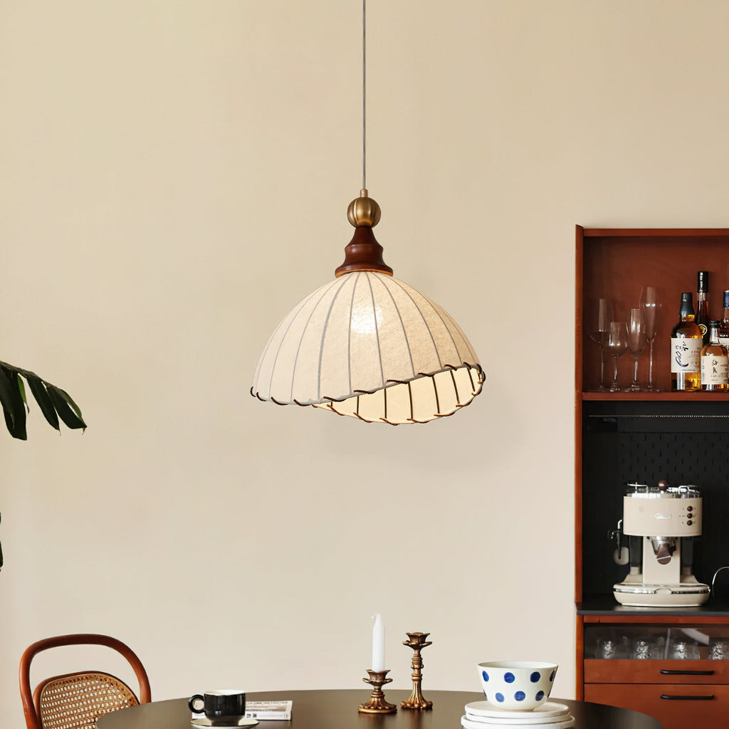 Beige Clérachic pendant light with a walnut cap, above a round table with a candle and a spotted bowl, beside a drinks shelf.