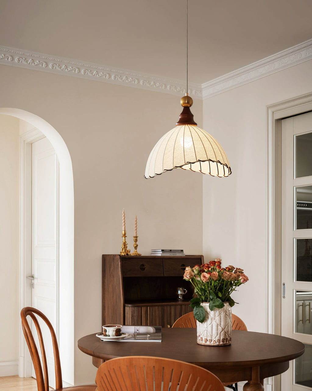Clérachic pendant light with a walnut cap hanging in a room with an arched door, over a dark round table set with flowers.