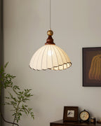 A Clérachic pendant light beside a leafy branch and a framed print, with a small clock and photo frame on a cabinet below.