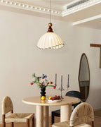 Beige Clérachic pendant light over a round stone table with cane chairs, flowers and candlesticks in a cornice-trimmed room.
