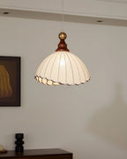 A Clérachic pendant light glowing in a grey room, with a patterned print on the wall and a black ceramic vase on a cabinet.