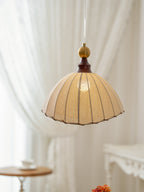 Clérachic pendant light seen against sheer white curtains, with its warm light showing through the beige pleated fabric.