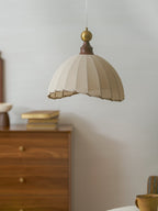 A beige Clérachic pendant light above a walnut chest of drawers with gold books, a small bowl and a stoneware mug.