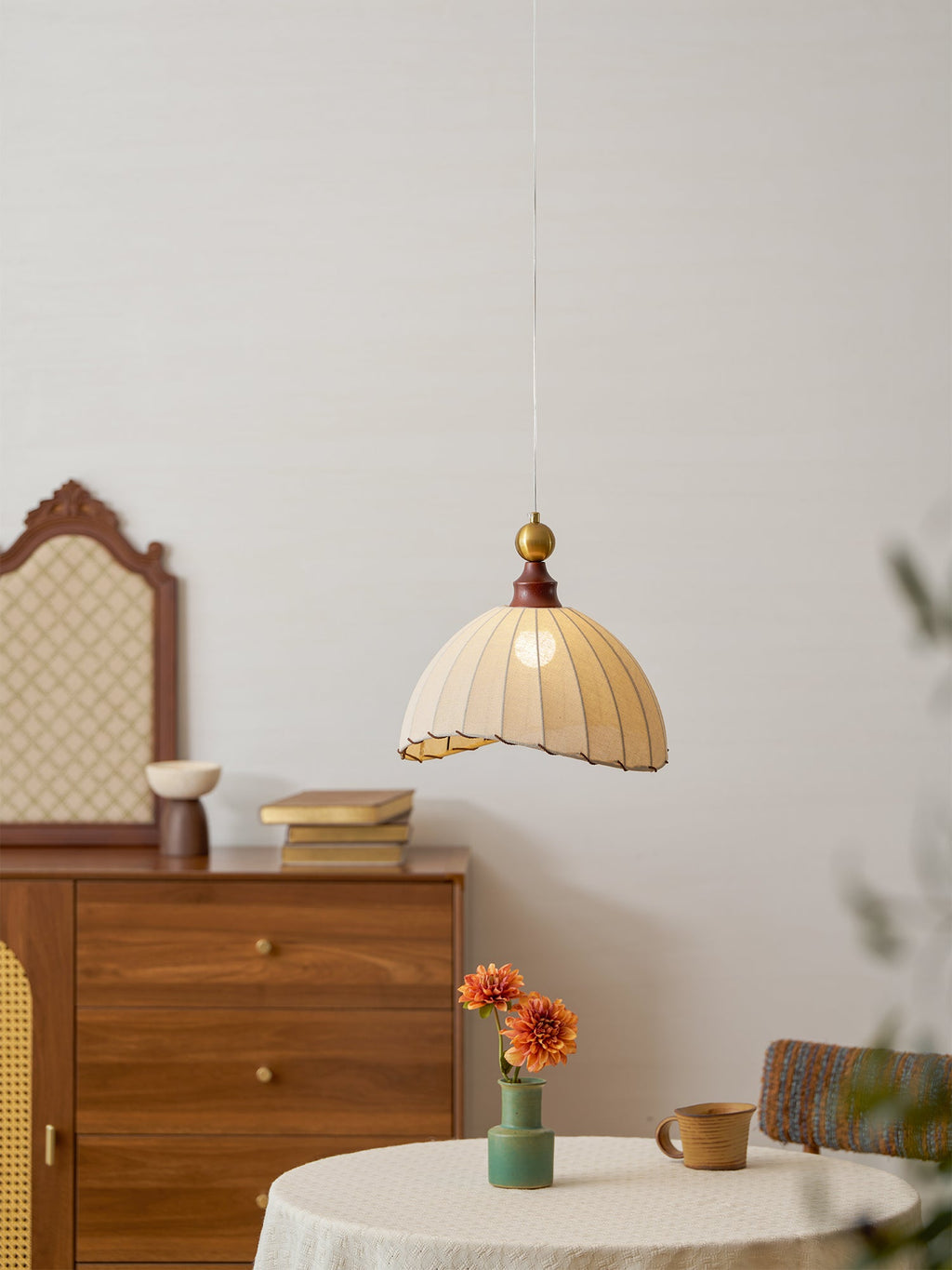 Clérachic pendant light seen from further back, lit above a round linen-covered table, with an arched mirror behind a chest.
