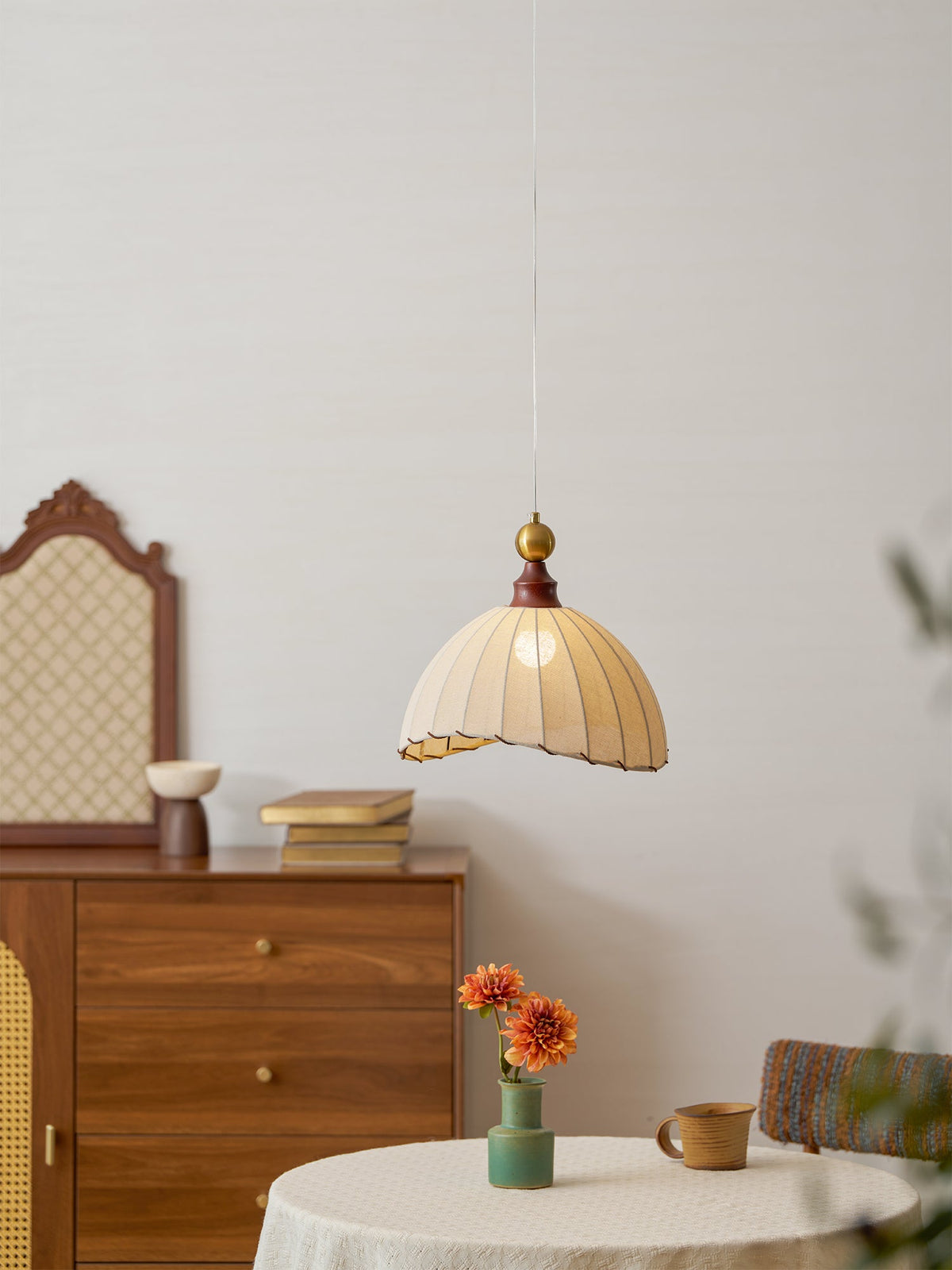 Clérachic pendant light seen from further back, lit above a round linen-covered table, with an arched mirror behind a chest.