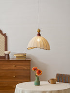A Clérachic pendant light with a walnut cap and brass ball, above a round table with orange flowers and a stoneware mug.