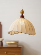 Close view of the scalloped lower edge and pleated beige fabric of this Clérachic pendant light, lit from inside.