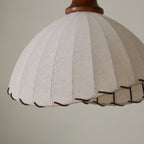 Close view of the pleated beige linen-look fabric and the twisted brown cord trim on the edge of this Clérachic pendant.
