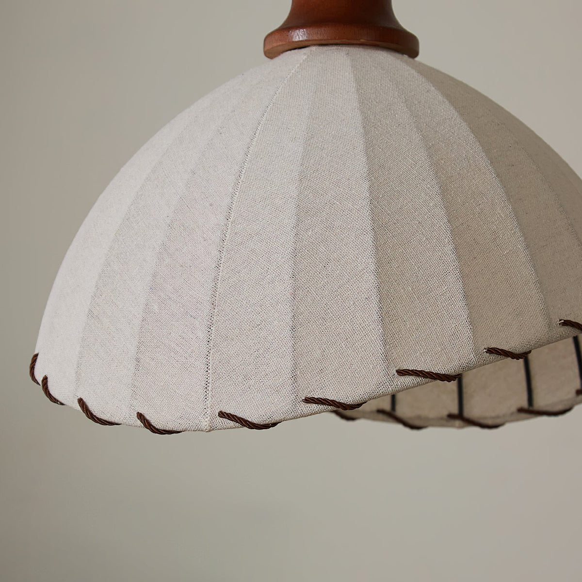 Close view of the pleated beige linen-look fabric and the twisted brown cord trim on the edge of this Clérachic pendant.