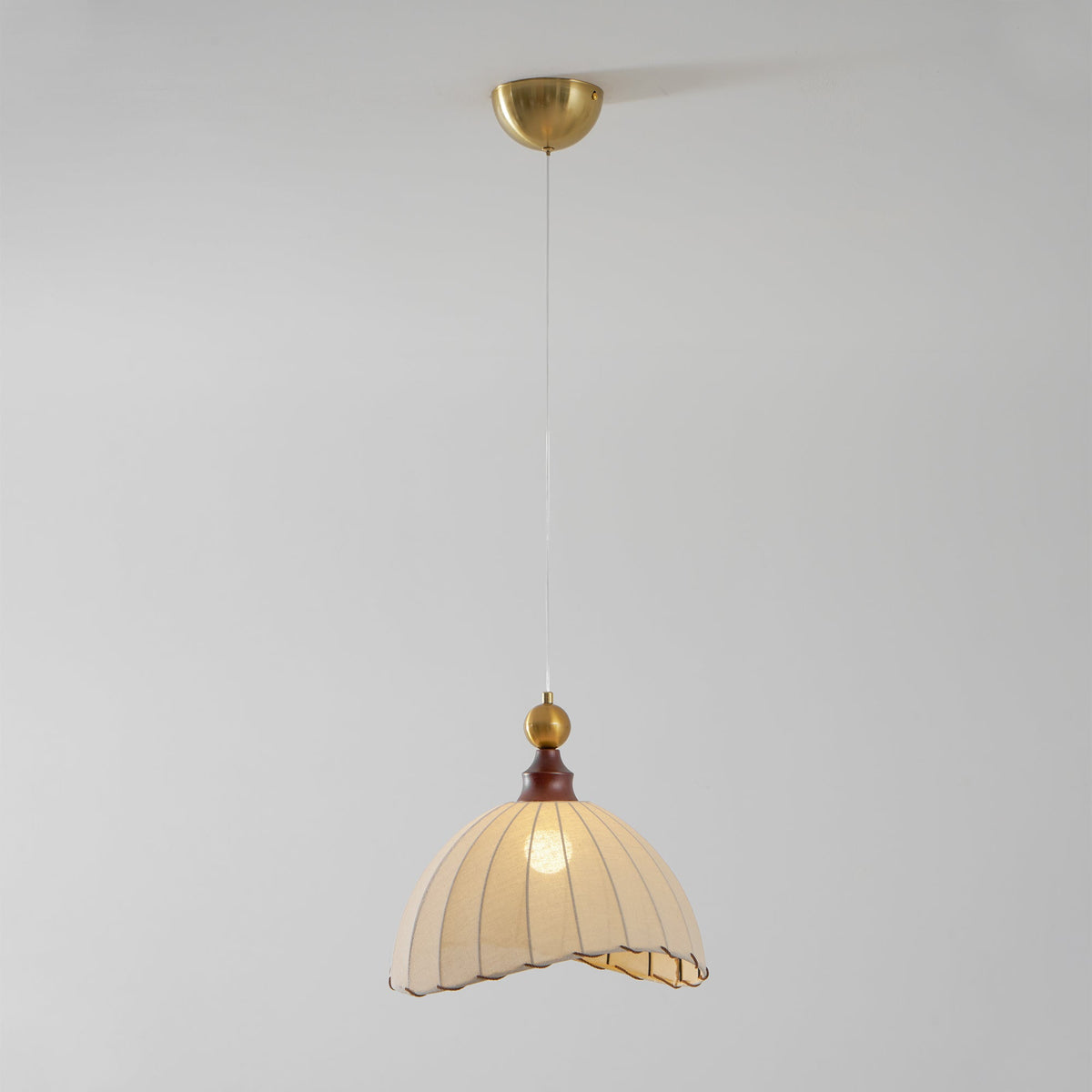 A Clérachic pendant light from below, with the brass canopy at the top and the shade glowing on a grey backdrop.
