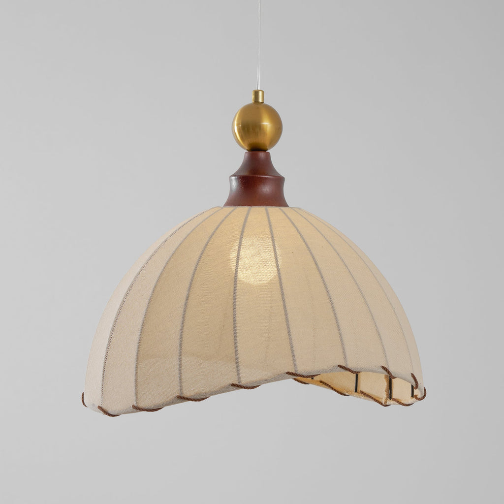 Clérachic pendant light with a walnut cap and brass ball, its pleated shade lit from inside against a grey backdrop.