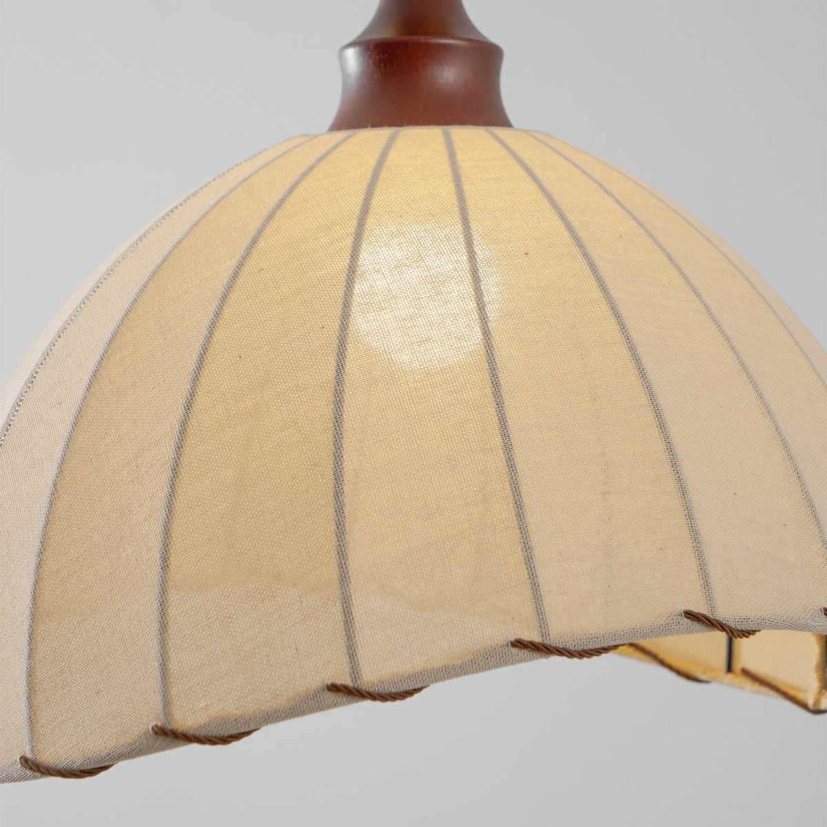 Close view of the inside glow and ribbed seams of the beige fabric shade on this Clérachic pendant light.