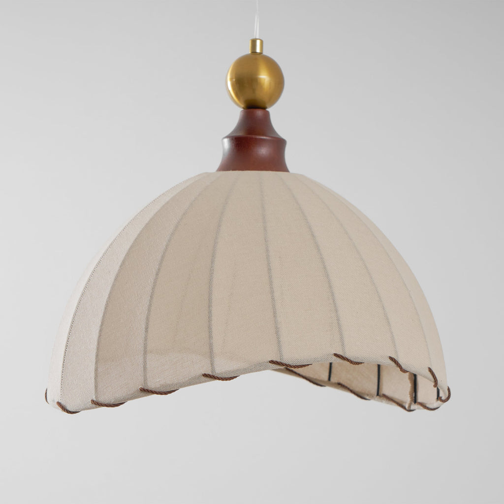 A Clérachic pendant light from a low angle, showing the pleated beige dome and brass ball against a pale grey backdrop.