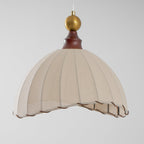 A Clérachic pendant light from a low angle, showing the pleated beige dome and brass ball against a pale grey backdrop.