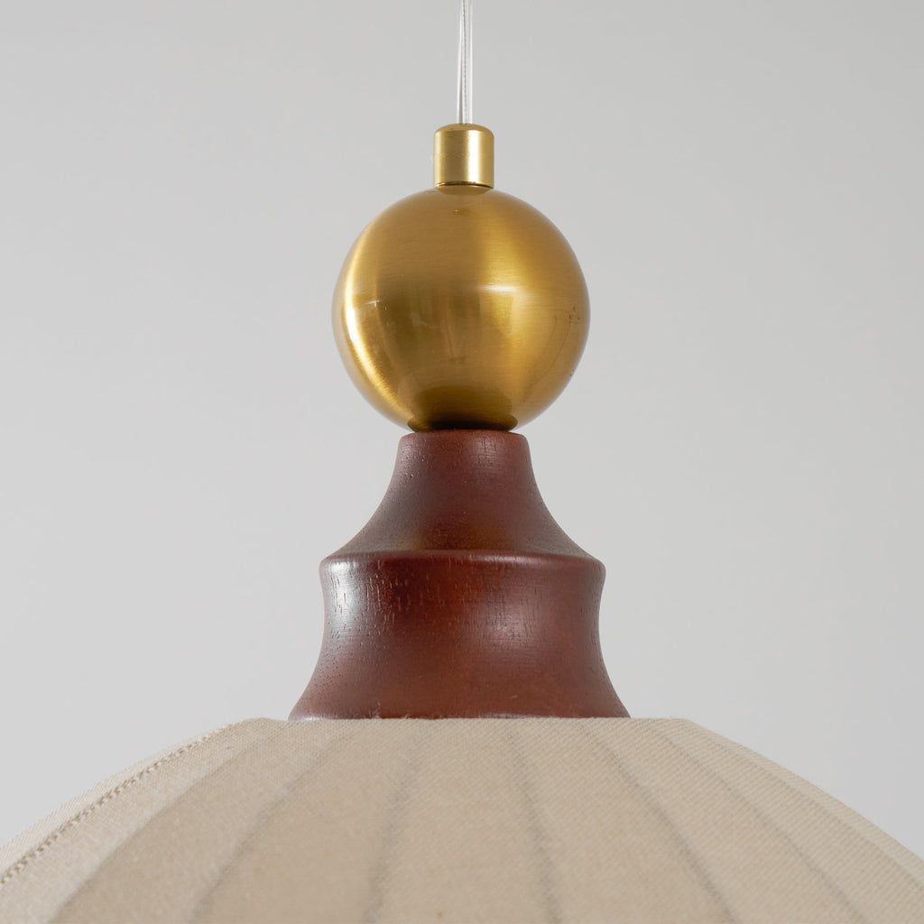 Close view of the brass sphere and turned walnut cap above the beige fabric dome of this Clérachic pendant light.