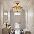 A Clérachic brass ceiling light with pleated glass hangs in a white panelled entrance hall above a marble console and a mirror.