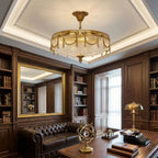 Brass ceiling light with a clear pleated shade, a Clérachic piece, glowing in a wood-panelled study with a leather sofa and desk.