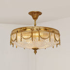 Lit brass ceiling light from Clérachic seen from below, its ribbed clear glass shade glowing warm against a pale wall.