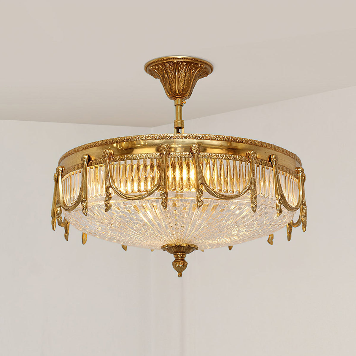 Lit brass ceiling light from Clérachic seen from below, its ribbed clear glass shade glowing warm against a pale wall.