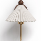 Close view of the pleated white shade and walnut ball finial on this Clérachic wall lamp, with the brass arm curving down below it.