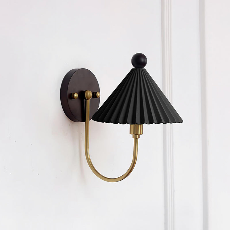 Shown here, a Clérachic wall lamp with a pleated black shade, a brass arm and a round dark backplate on a white wall.