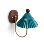 This Clérachic wall lamp has a pleated blue-green shade, a curved brass arm and a round walnut backplate on a white wall.