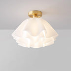 The Clérachic Pleated Petal Ceiling Light seen at an angle in a grey studio, its brass canopy holding the ruffled acrylic shade.