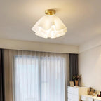 The Clérachic Pleated Petal Ceiling Light lighting a bedroom corner with grey curtains and a white chest of drawers below it.