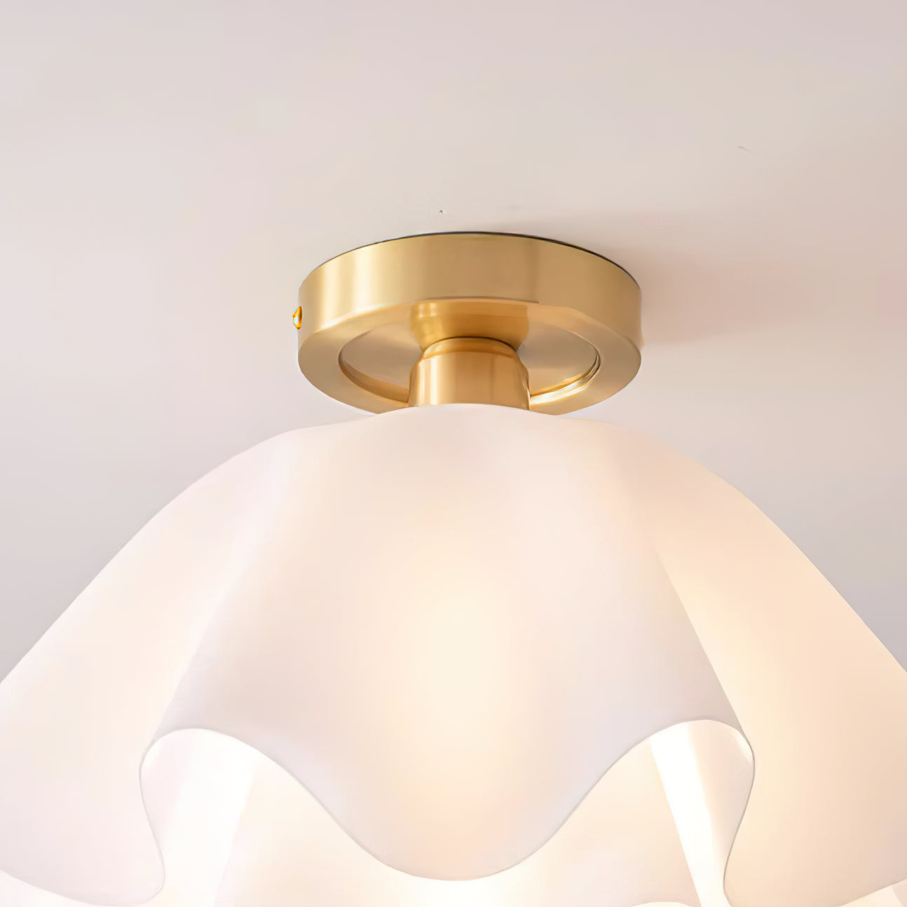 Close view of the brass canopy plate on the Clérachic Pleated Petal Ceiling Light, fixed flat to the ceiling above the glowing shade.