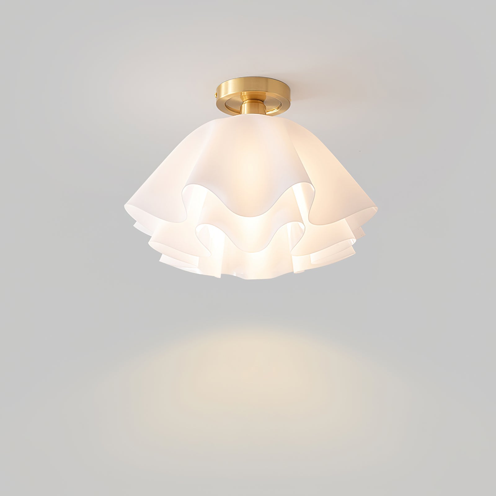 The Clérachic Pleated Petal Ceiling Light switched on against a grey wall, throwing a soft pool of warm light beneath it.