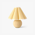 A Clérachic ceramic table lamp with a beige ball base and a pleated yellow plaid shade, on a plain white backdrop.