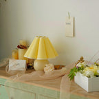 Pictured here, a Clérachic table lamp with a pale yellow pleated shade stands on a mint-green cabinet, with flowers and candles around it.