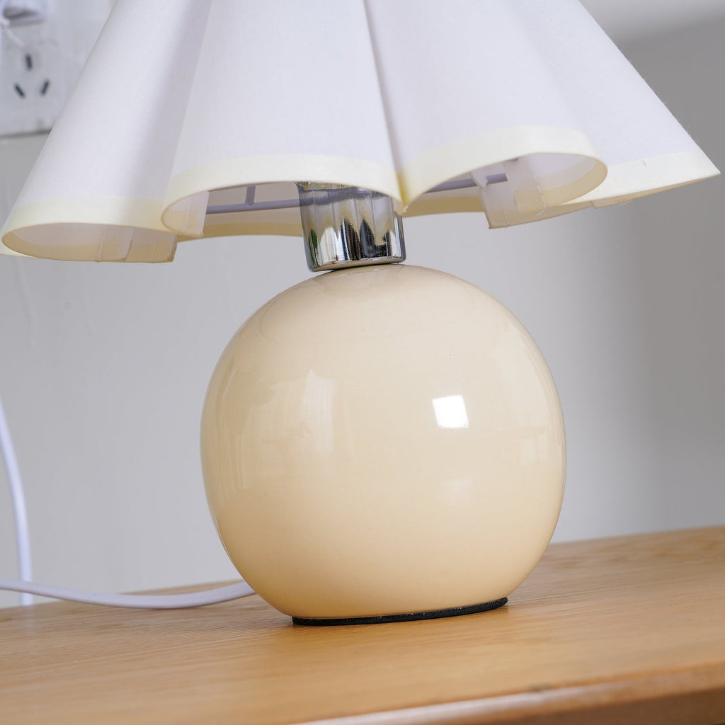 Close view of the glossy beige ceramic ball base and chrome neck of this Clérachic table lamp, under a white pleated shade.