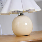Close view of the glossy beige ceramic ball base and chrome neck of this Clérachic table lamp, under a white pleated shade.