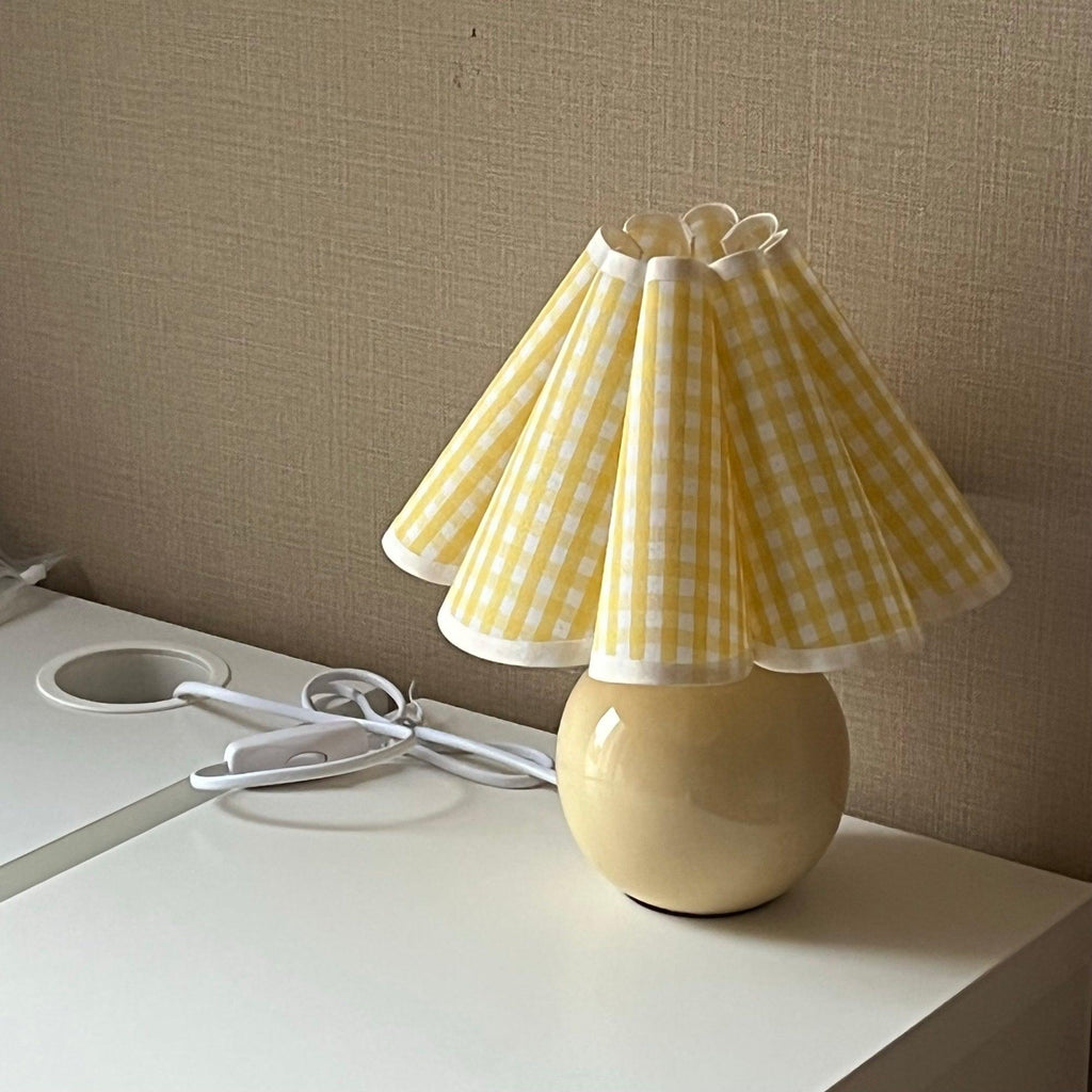 Seen from the side, this Clérachic table lamp with a yellow plaid pleated shade stands on a white desk against a taupe wall.
