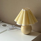 Seen from the side, this Clérachic table lamp with a yellow plaid pleated shade stands on a white desk against a taupe wall.