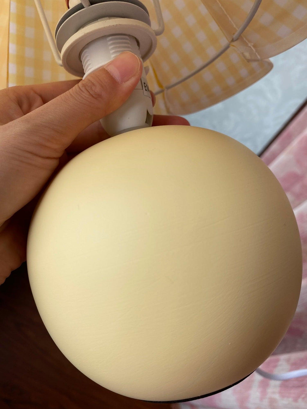 A hand holds the round ceramic base of this Clérachic table lamp, showing the bulb holder under a yellow plaid shade.