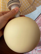 A hand holds the round ceramic base of this Clérachic table lamp, showing the bulb holder under a yellow plaid shade.