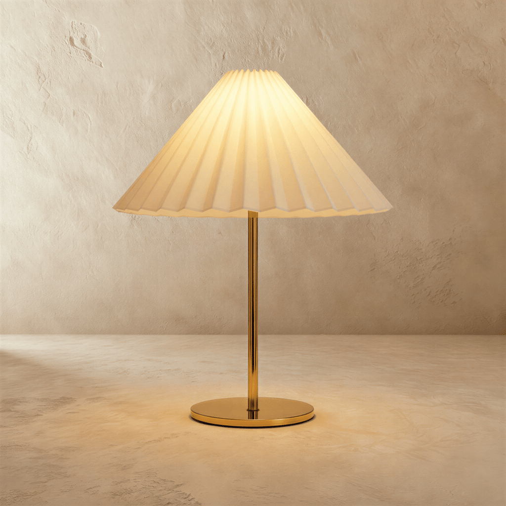 Clérachic table lamp with a cream pleated conical shade, glowing warm on a slim brass stem and round brass base against limewash.