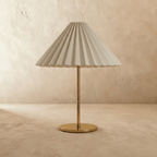 Clérachic table lamp with a pale grey-white pleated conical shade on a slim brass stem and flat round brass base, unlit, on limewash.