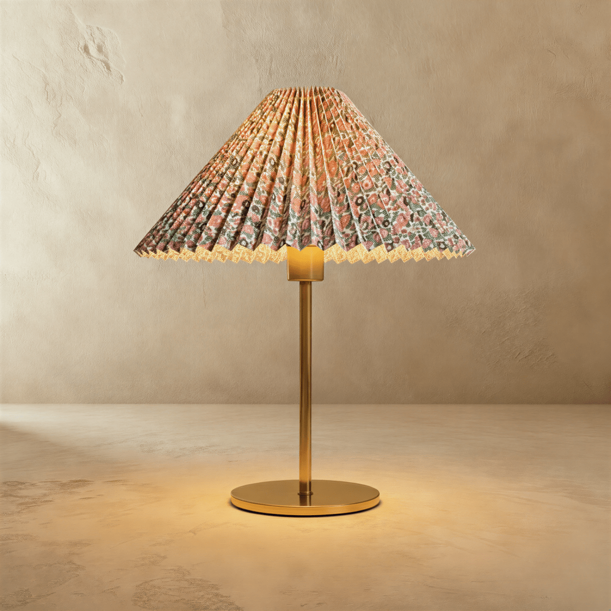 Clérachic table lamp with a pleated conical shade in a pink and green floral print, on a slim brass stem and round base, glowing warm.