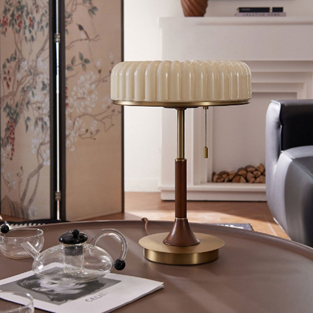 Pleated shade and pull chain of this Clérachic table lamp, set on a round coffee table beside a glass teapot and a folding screen.