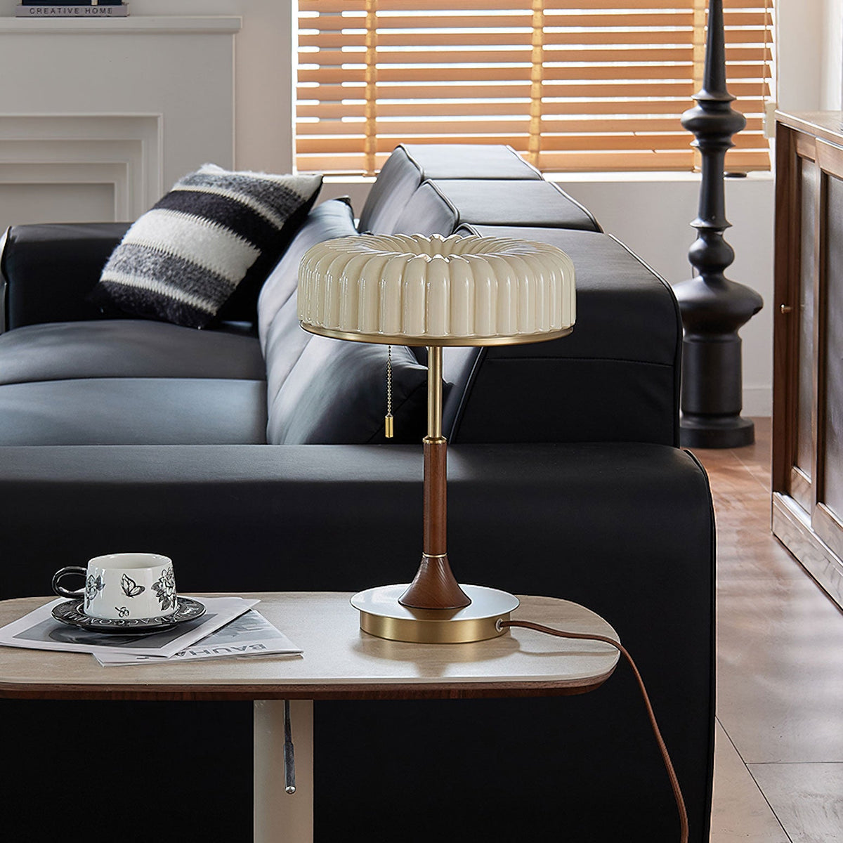 Shown here, a Clérachic table lamp on a small side table next to a black leather sofa, with a cup and saucer resting on a magazine.