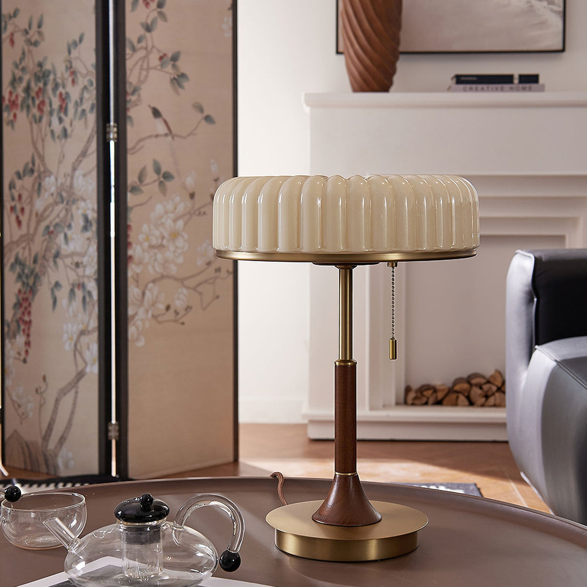 Close framing of this Clérachic table lamp on a coffee table in front of a floral folding screen, its pull chain hanging beside the stem.