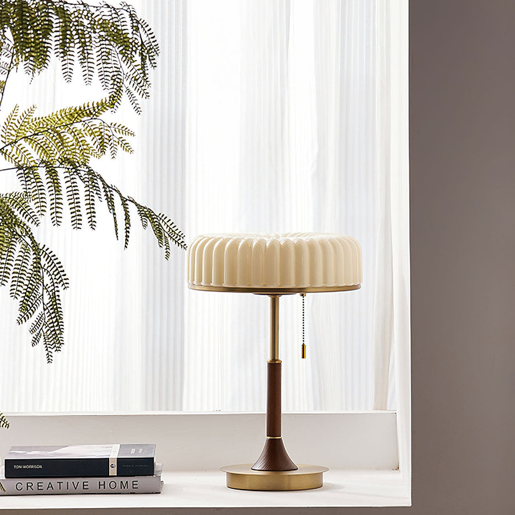 A Clérachic table lamp on a white windowsill with sheer curtains behind it, a feathery plant to the left and two books at its side.